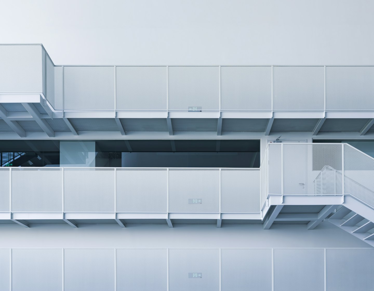 Extérieur d'un bâtiment moderne avec balcons et escalier en métal blanc perforé.