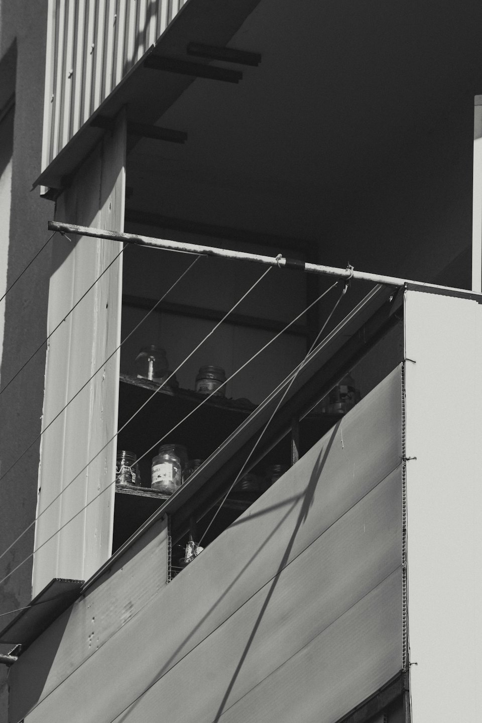 Des bocaux en verre sur des étagères derrière la rambarde d'un balcon avec une corde à linge.
