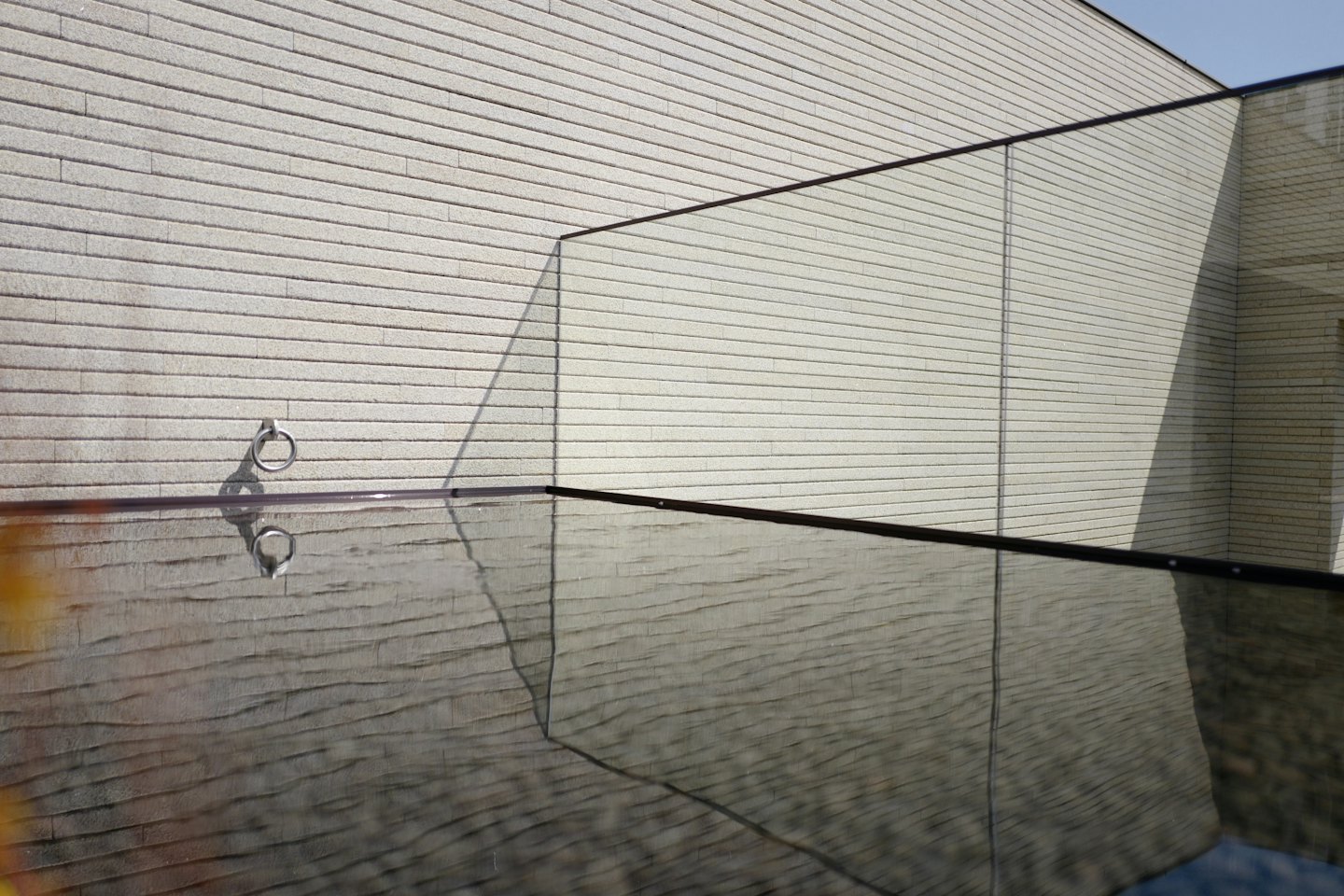 Des ombres géométriques d'une rambarde en verre tombent sur un mur texturé.