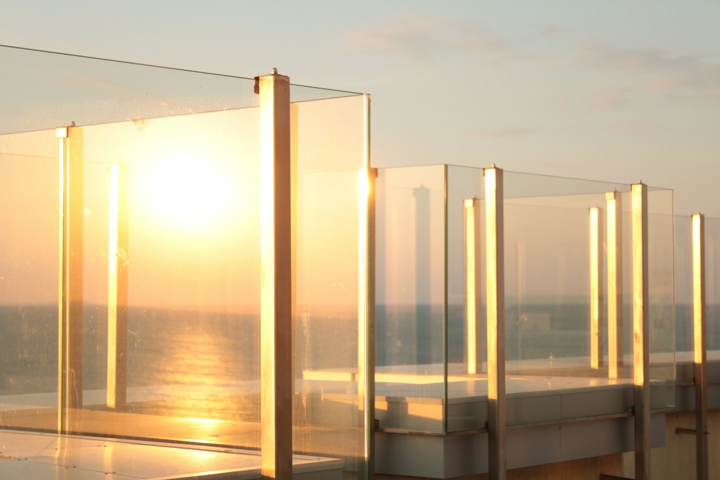 Garde-corps de balcon moderne en verre donnant sur l'océan au coucher du soleil.