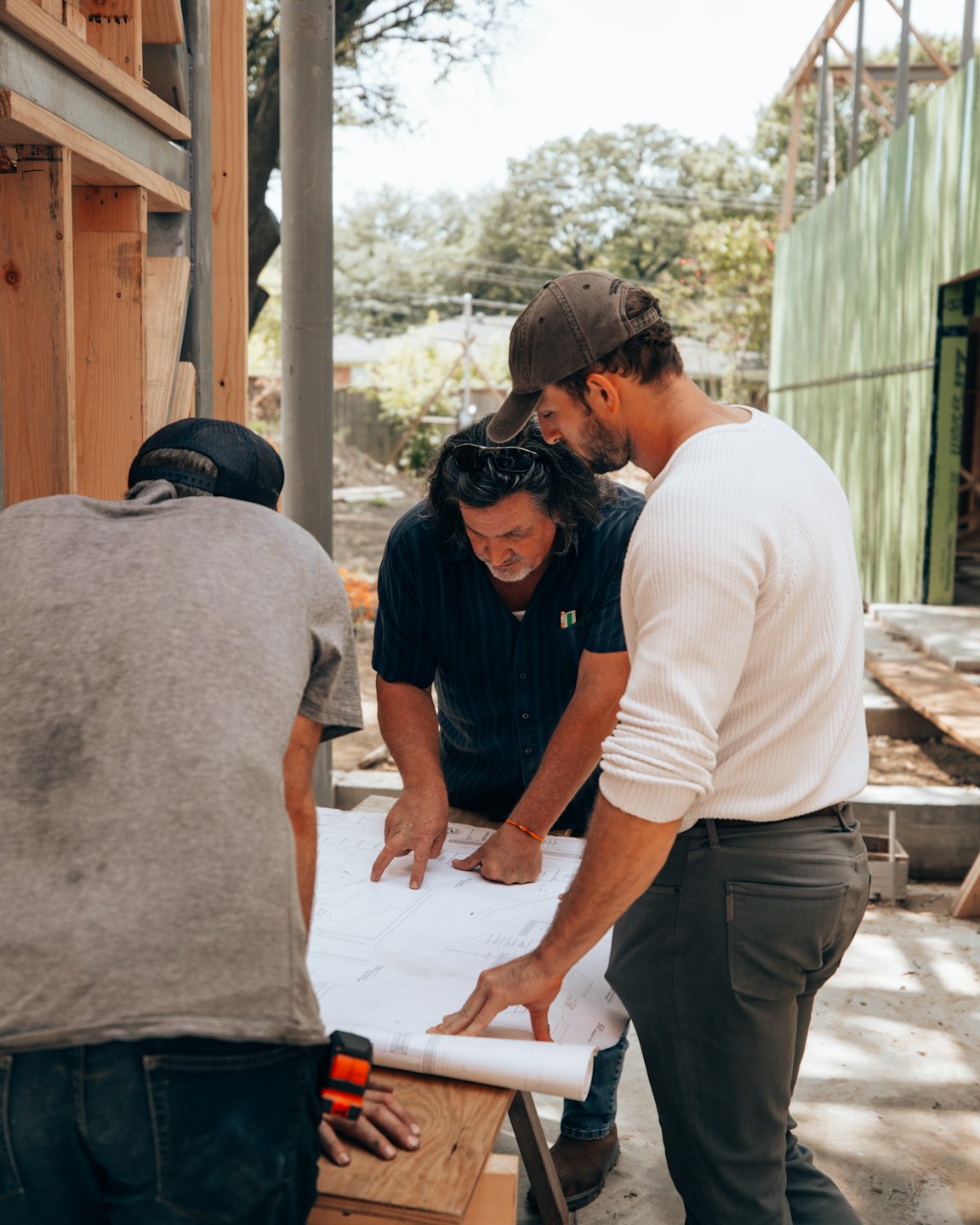 Trois professionnels de la construction examinent des plans sur un chantier extérieur.