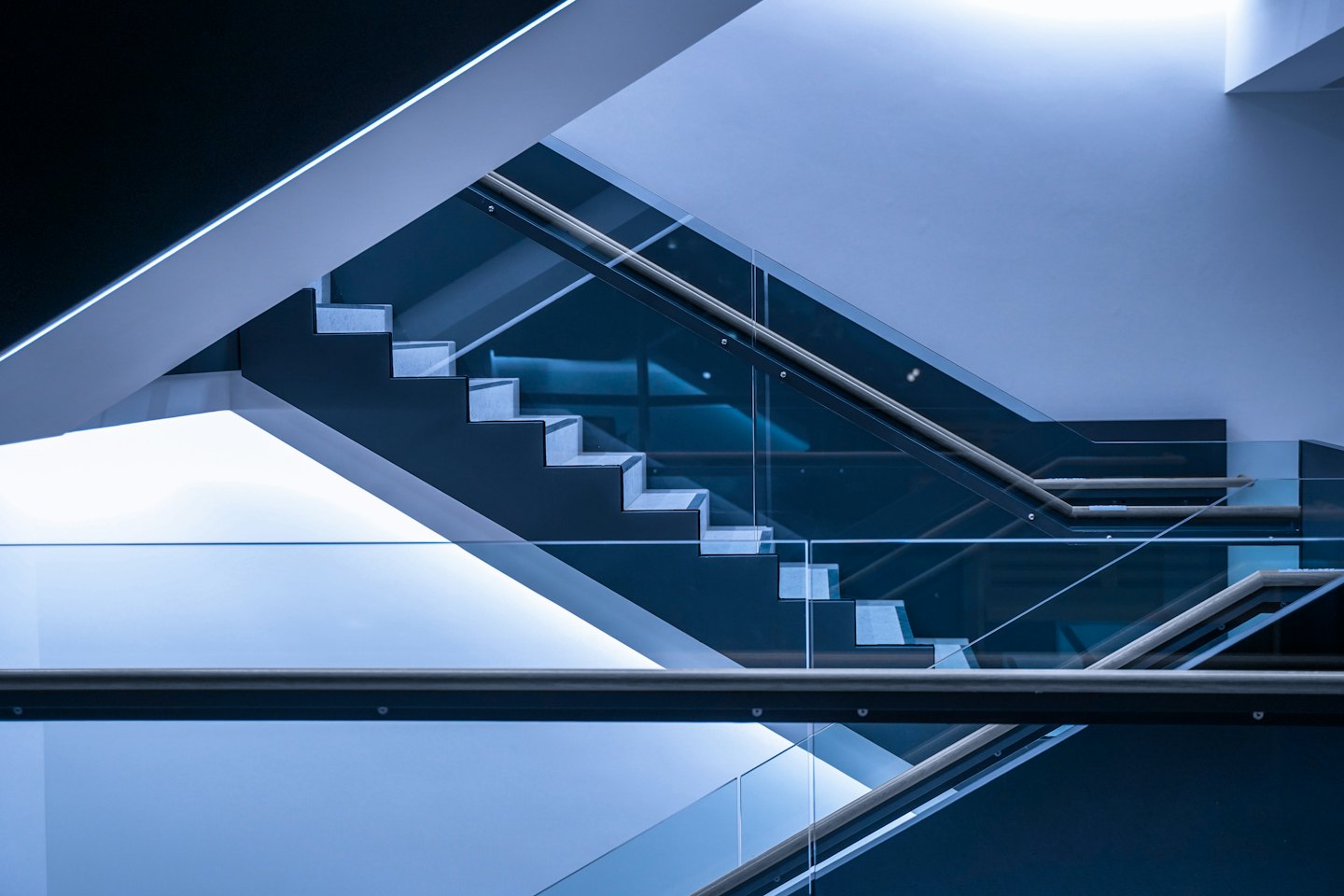 Escalier moderne avec marches en métal sombre et rampes en verre.